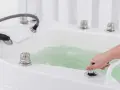 Dłoń reguluje strumień wody w wannie, przygotowując relaksujący masaż wirowy.