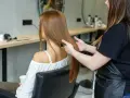 Fryzjerka wykonuje degażowanie włosów klientce w salonie. Długie, proste, rude włosy są delikatnie przeczesywane.