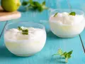 Due bicchieri di sorbetto al limone senza albume, guarniti con menta fresca, su un tavolo di legno blu.