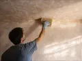 Hombre con guante azul usa esponja para sanear pared con textura.