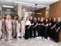 Grupa uśmiechniętych dentystów i personelu medycznego w jasnych i ciemnych uniformach stoi w nowoczesnym gabinecie.