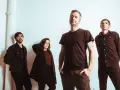 Quatre musiciens, un groupe rock canadien francophone, posent devant un mur blanc.