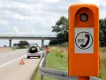 Ihr Fahrzeug ist auf der Autobahn liegen geblieben. Eine Frau in Warnweste steht neben dem offenen Kofferraum, ein Warndreieck liegt auf der Fahrbahn. Eine Notrufsäule steht im Vordergrund.