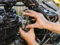 Ręce mechanika regulują gaźnik motocykla, pokazując, jak działa ssanie.