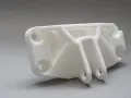 A white, complex SLS part with multiple holes and support structures, ready for assembly.