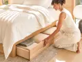 Une femme range des draps dans un tiroir de lit en bois.