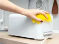 Eine Hand wischt mit einem gelben Tuch über einen weißen Toaster. So einfach ist das Toaster reinigen für ein blitzsauberes Ergebnis.