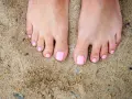 Stopy na piasku z różowym, modnym pedicure. Idealne na lato.