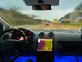 Widok z kabiny samochodu jadącego autostradą. Na desce rozdzielczej tablet z nawigacją, a obok niego system rozpoznawania znaków drogowych.