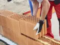 Murowanie ścian z porothermu. Budowlaniec w rękawicy zakłada kolejny pustak na pianę montażową.