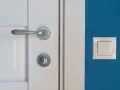 Eleganckie, metalowe klamki do białych drzwi idealnie komponują się z niebieską ścianą i białym włącznikiem.