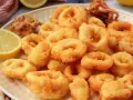 Plato de calamares a la romana dorados y crujientes, servidos con rodajas de limón fresco.