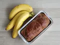 Gotowy proteinowy chlebek bananowy w formie, obok pęk dojrzałych bananów.