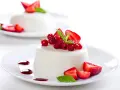 Deliciosa panna cotta cremosa adornada con fresas, grosellas rojas y menta fresca.