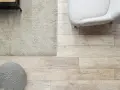 Elige el color del suelo de una casa con este suelo de madera clara, alfombra beige y puf gris.