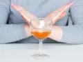Ręce skrzyżowane nad kieliszkiem z bursztynowym płynem. Pytanie: po jakim czasie od zastrzyku można pić alkohol?