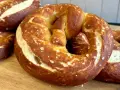 Frisch gebackene, goldbraune sauerteig brezeln mit grobem Salz bestreut, liegen auf einem Holzbrett.