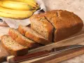 Pyszny, domowy chlebek bananowy, pokrojony na kromki, leży obok dojrzałych bananów na desce.