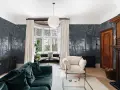 Sala con papel pintado de bosque, sofá verde, sillón beige y chimenea de madera. Ideas de como poner papel pintado para transformar tu hogar.