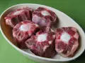 Trozo de rabo de ternera crudo en un cuenco, con el hueso central visible.