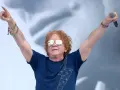 Wokalista Simply Red z uniesionymi rękami, trzymający mikrofon. Ma charakterystyczne rude włosy i okulary przeciwsłoneczne.