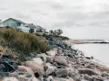 Häuser am Hang über einem steinigen Strand. Ein ruhiger Ort, der zu den Fehmarn Geheimtipps zählt.