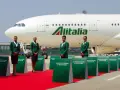 Cztery stewardessy w zielonych uniformach stoją na czerwonym dywanie przed samolotem Alitalia.