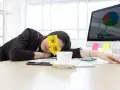 En kvinna sover vid sitt skrivbord med post-it-lappar som föreställer ögon på ögonlocken. Det är uppenbart att hon tycker det är tråkigt på jobbet.