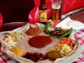 Tradycyjna kuchnia etiopska na płaskim chlebie injera, z różnymi gulaszami, warzywami i papryczkami. Obok piwo.