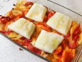 Cuatro porciones de bacalao al horno reposan sobre patatas y pimientos asados en una fuente de vidrio.