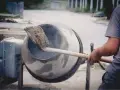 Robotnik miesza łopatą mieszankę cementową w betoniarce.
