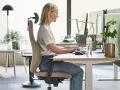 En kvinna sitter ergonomiskt vid ett skrivbord och arbetar vid datorn.