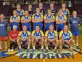 Drużyna SPR Chrobry Głogów pozuje do zdjęcia. Zawodnicy w żółto-niebieskich strojach sportowych, trenerzy i jedna kobieta.