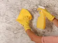 Manos con guantes amarillos limpian paredes con un paño y spray.