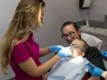 Dentystka bada zęby chłopca, podczas gdy jego mama go wspiera. Zwracają uwagę na zdrowie dziąseł, by zapobiec recesji dziąseł.