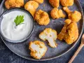 Knusprige Blumenkohl Nuggets aus dem Ofen, goldbraun paniert und mit Sesam bestreut, serviert mit einem cremigen Dip.