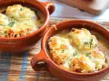 Dos cazuelas de barro con sopa de cebolla gratinada con queso y hierbas.