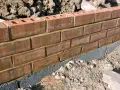 Ceglana ściana ogrodzenia z widoczną warstwą izolacyjną, która stanowi alternatywę dla tradycyjnej podmurówki.