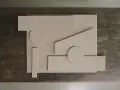 Abstrakt komposition med geometriska former i ljusbeige akrylfärg, arrangerade på en mörk träyta.