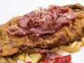 Cachopo asturiano rebozado con jamón serrano encima, acompañado de patatas fritas y pimientos rojos.