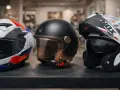 Tre caschi da moto in primo piano: uno bianco con grafiche rosse e blu, uno nero stile retrò con interni in pelle, e uno bianco e nero con visiera scura. La calotta del casco è il dettaglio che cattura l'attenzione.