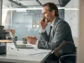 Biznesmen w garniturze rozmawia przez telefon, pracując przy laptopie. To typowy dzień w życiu CEO, co to znaczy być liderem.