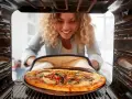 Uśmiechnięta kobieta wyjmuje z piekarnika pyszną, gorącą pizzę. Właśnie skończyła piec pizzę i jest gotowa do jedzenia.