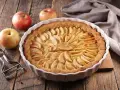 Torta di mele umida e soffice, con mele fresche e un pelapatate su un tavolo di legno rustico.