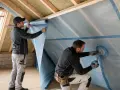 Operai installano membrana traspirante per tetto. La permeabilità al vapore dei materiali è fondamentale per l'isolamento.