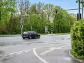 Ein dunkles Auto fährt auf nasser Straße an einer roten Ampel vorbei, neben der ein ampel blitzer steht.