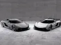 Dwa lśniące Koenigsegg Jesko, jeden szary, drugi srebrny, stoją obok siebie na betonowym tle, gotowe do wyścigu.