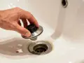 A hand holds a bathtub drain stopper, showing how to remove bathtub drain parts for cleaning or repair.