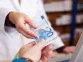 Eine Person in einem weißen Kittel reicht einen 20-Euro-Schein. Möglicherweise zur Bezahlung von Krankengymnastik Kosten.