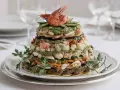 Un maestoso cappon magro a strati, con gamberi, verdure e salsa verde, guarnito con prezzemolo fresco.